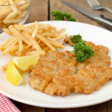 authentic german pork schnitzel served with fries, a wedge of lemon, and parsley on a white plate