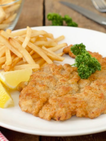 authentic german pork schnitzel served with fries, a wedge of lemon, and parsley on a white plate