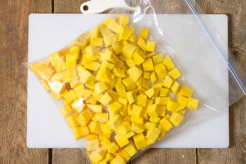 Diced butternut squash in a clear re-sealable food grade bag on a white cutting board.