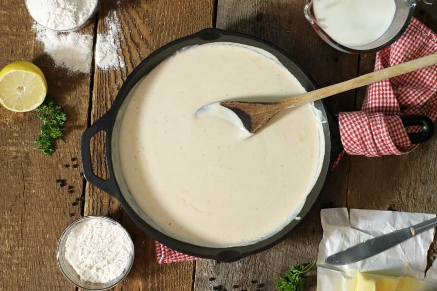 overhead shot of bechamel sauce in a cast iron pan, surrounded by various ingredients.