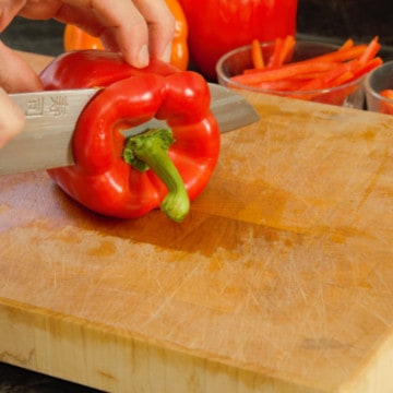 slicing into a red pepper on a wooden cutting board