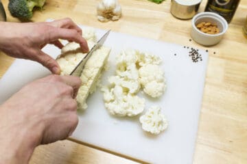 Roughly chopping cauliflower for soup on a white cutting board with a large chefs knife.