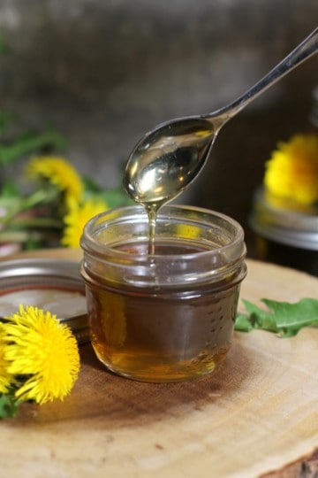 golden yellow dandelion syrup dripping of a spoon into a mason jar