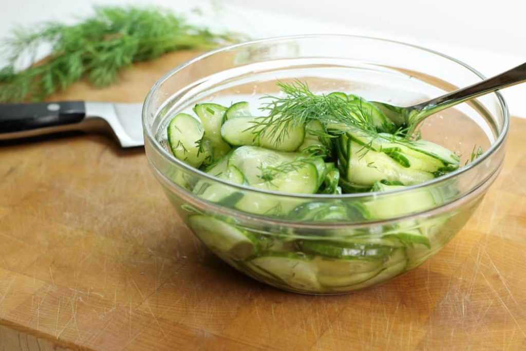 german cucumber salad garnished with dill in a glass bowl