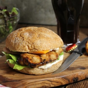 a fully assembled marinated grilled chicken burgermon a wooden serving board