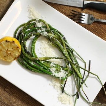Grilled garlic scapes with grilled lemon and parmesan on a white plate