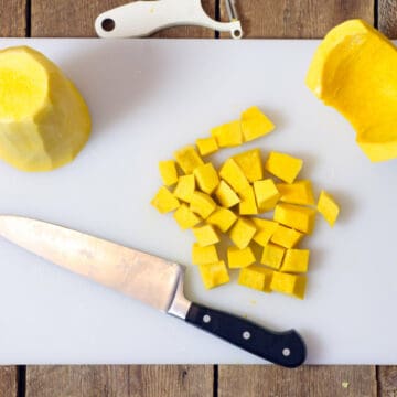 a top down view of a peeled butternut squash cut into various shapes on a white cutting board.