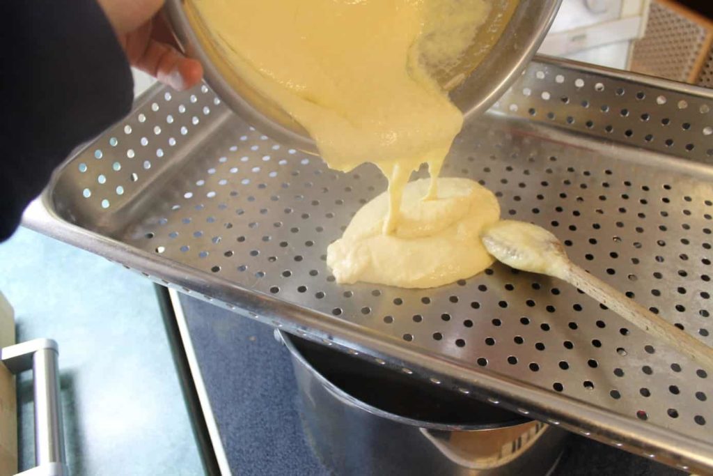 Spatzle dough being poured into a perforated pan over a pot of boiling water