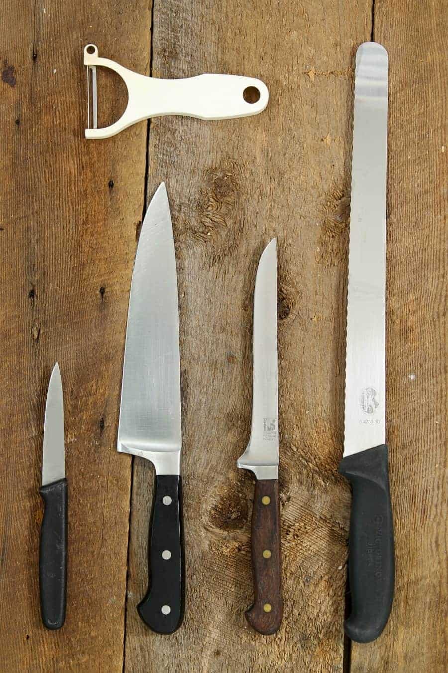 vertical image of a paring knife, chefs knife, boning knife, and serrated slicer on a wooden table top