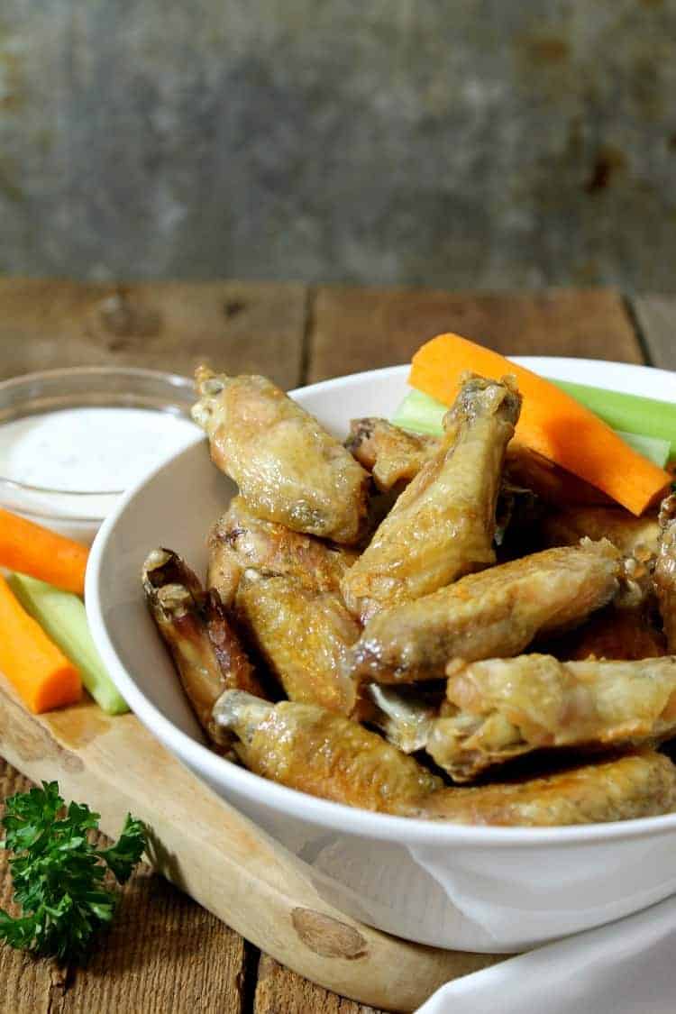 crispy oven baked chicken wings in a white bowl served with carrot and celery sticks