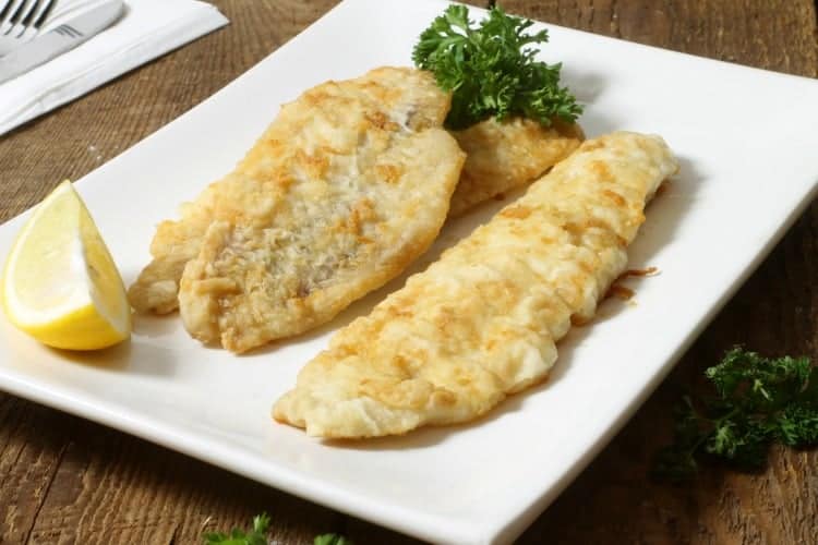 pathree pan fried pieces of haddock in a white plate with lemon wedges and parsley