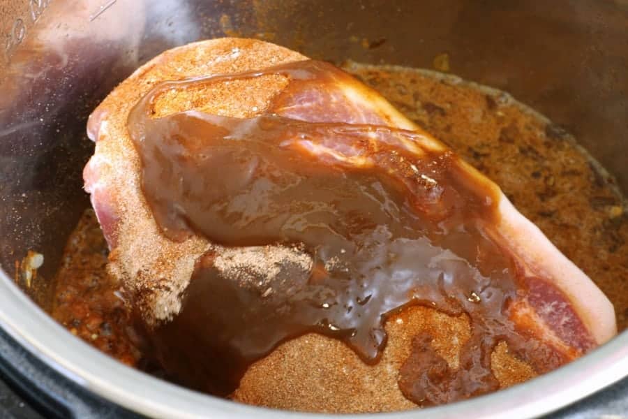 a pork shoulder with various spices in a instant pot ready to be cooked.
