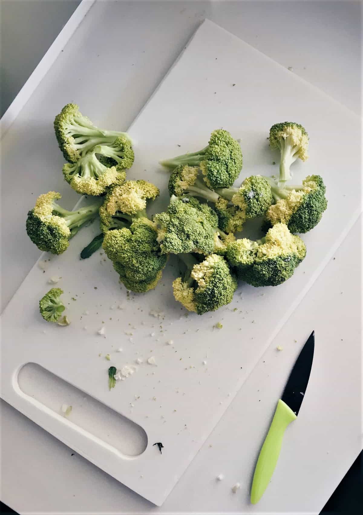 broccoli cut into small florets on a white cutting board