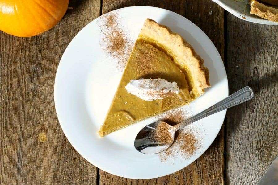 an overhead view of a slice of dairy free pumpkin pie on a white plate garnished with cinnamon and coconut cream