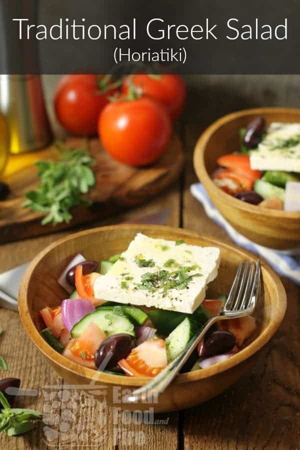 A bowl of traditional Greek salad also known as horiatiki on a wooden table surrounded by various ingredients