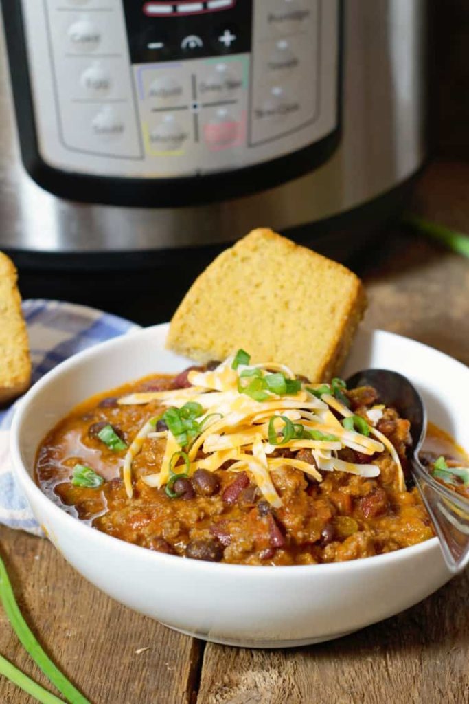 vertical image of instant pot chili served in a white bowl with cornbread