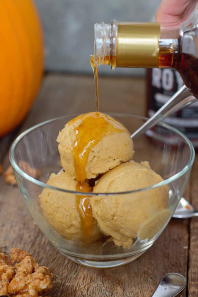 maple syrup being poured over a bowl of freshly scooped pumpkin ice cream