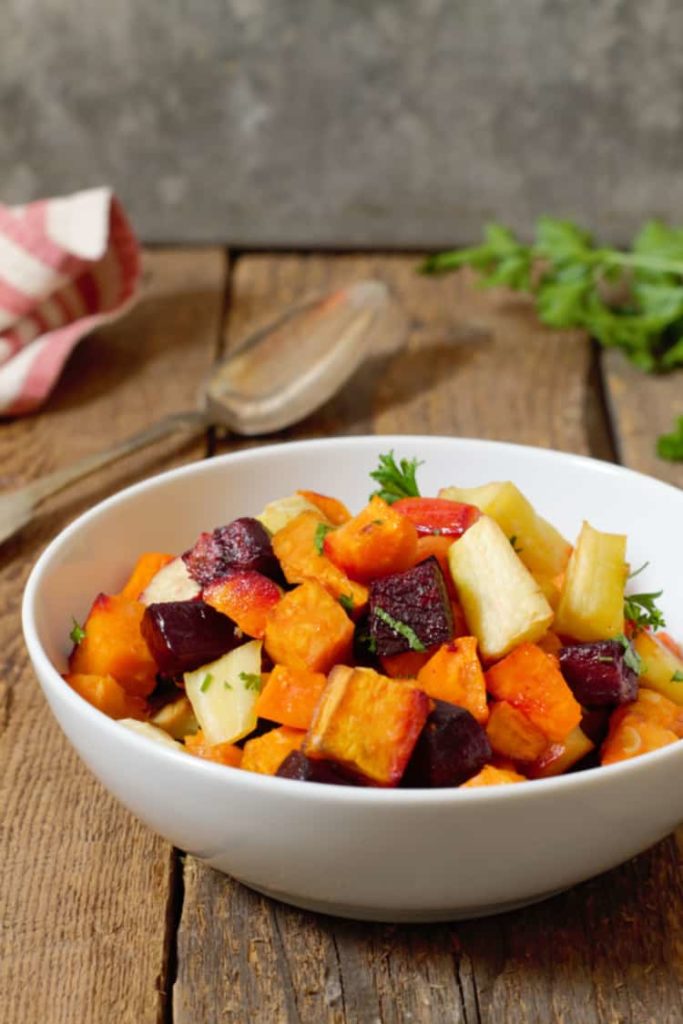 oven roasted root vegetables served in a white bowl on a rustic barn board background